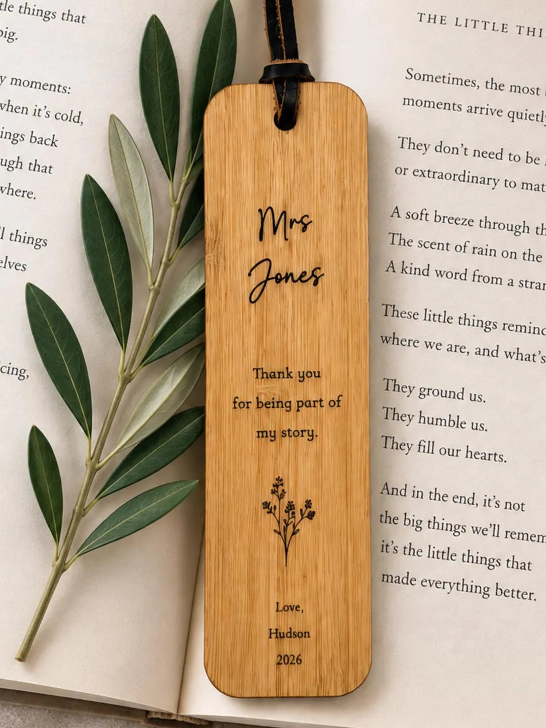 A personalised bamboo book mark with the name 'Mrs. Jones' and a thank you message, displayed on an open book next to an olive branch sprig.