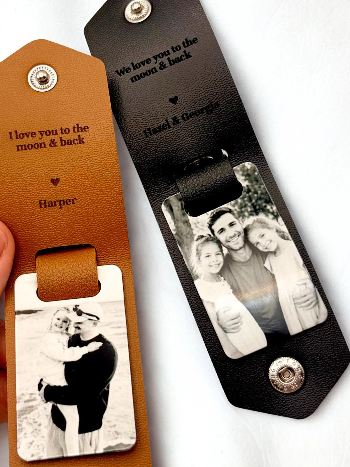Two personalized leather luggage tags with photo inserts, one in tan leather and one in black leather, shown on a white background with a hand holding the tan version.